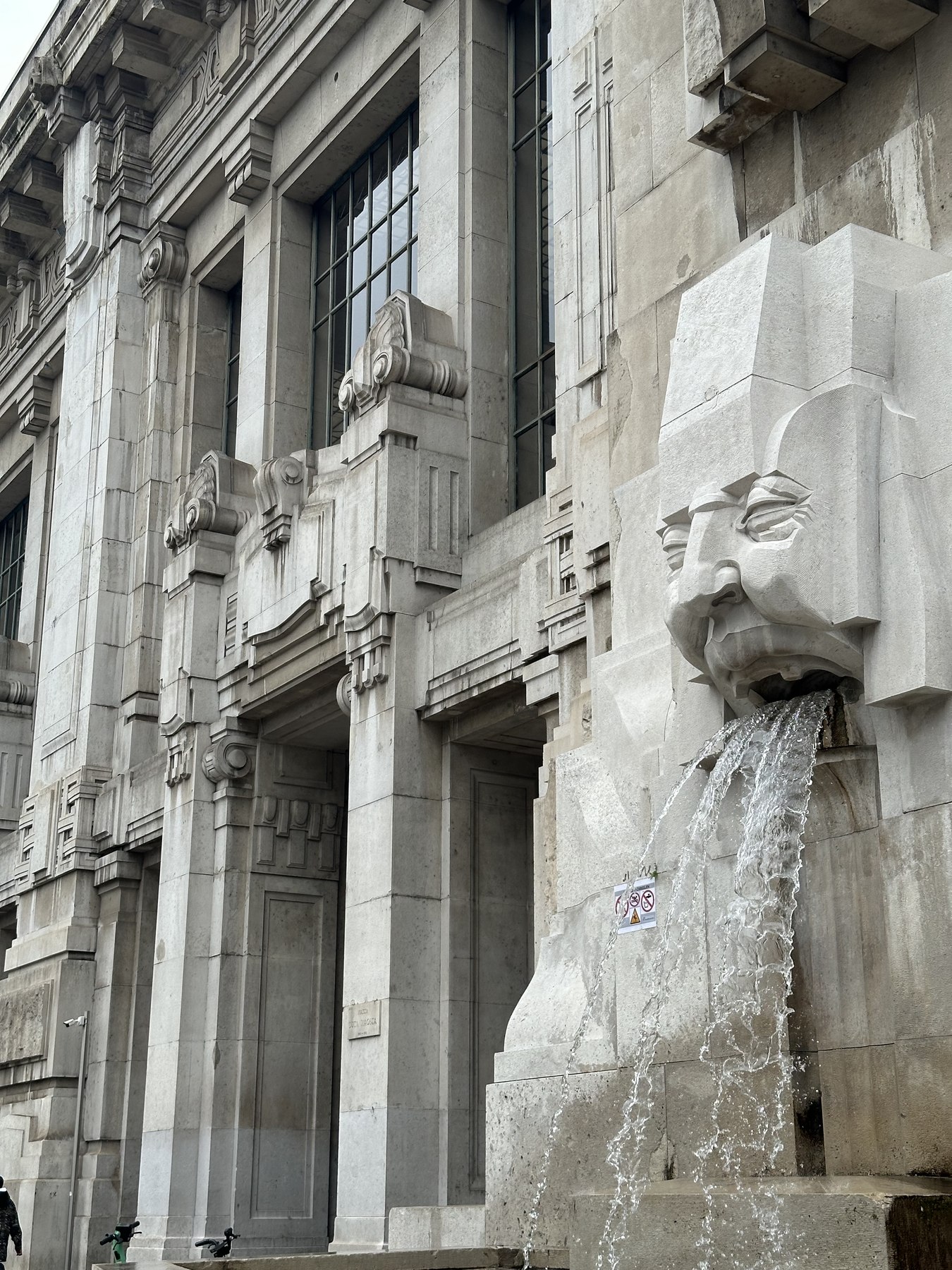 Fontana con leone in pietra e dettagli monumentali della facciata di Milano Centrale